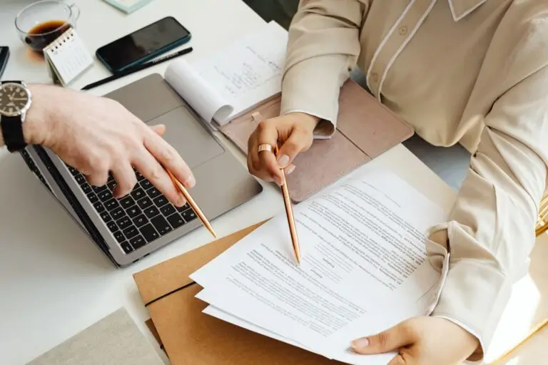 Twee personen bekijken documenten naast een laptop